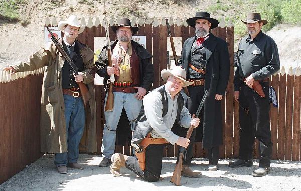 Five armed cowboys in period garb in front of the stockade entrance